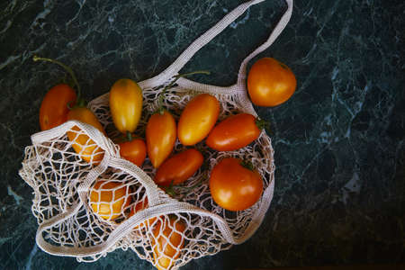 Harvest bright colorful tomatoes in eco shopping bag with reflection background. Zero waste. eco...