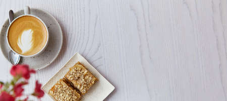 Natural turkish baklava and cup of cappuccino on wooden table outdoor. Pink flowers decorations in the cafe terrace. coffee break. Extra wide banner. copyspace.の写真素材