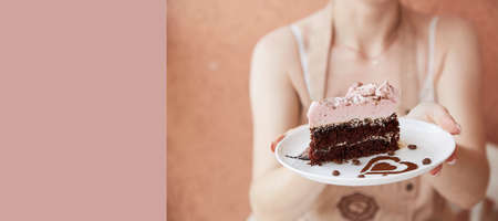 Woman is holding fruit chocolate piece of cake and cup of cappuccino on wooden table outside in the...