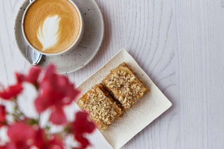 Natural turkish baklava and cup of cappuccino on wooden table outside. coffee break. Pink flowers decorations in the cafe terraceの写真素材
