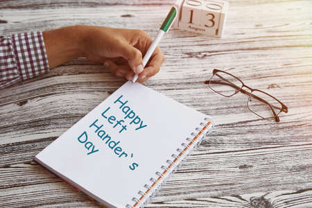 Man uses his left hand to wright in a notebook. Glassess and calendar with 13th of August - Day of...
