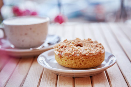 Natural caramel sweet donut with cappuccino on wooden table. Aesthetic coffee time outside at the terraceの写真素材