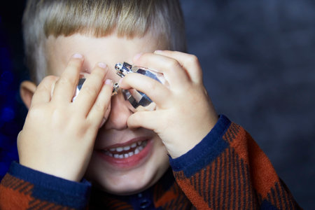 Portrait of cute joyful toddler. Boy plays with Christmas tree disco ball among Christmas...