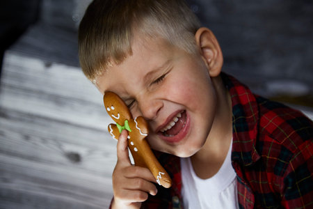Adorable cheerful child hides behind Christmas gingerbread and makes a funny face expression....
