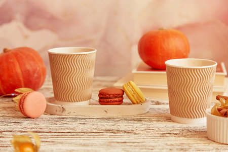 Aesthetics cardboard cups with pumpkin latte. Seasonal couple breakfast with coffee and macaroons among pumpkins. Cozy autumn atmosphere.の写真素材