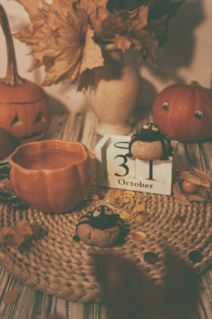 Dark autumn Halloween cookies in shape of spider and cup of tea among pumpkins and Jack o lantern. October 31 on calendarの写真素材