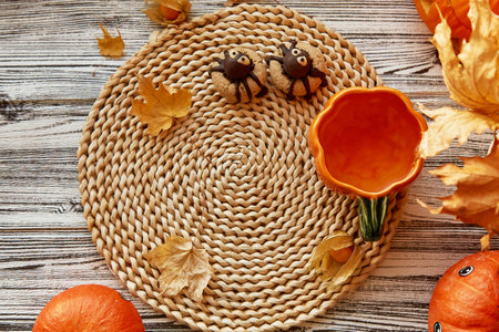 Funny Halloween mock up with spider cookies and cup of tea in shape of pumpkin near among fragrant leavesの写真素材