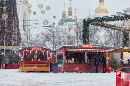 Kyiv, Ukraine - January, 2022: Christmas market at snowy day - temple, Christmas tree, carousel, people, shops and decorations. Festive holidays before war.のeditorial素材
