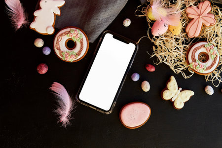 Mockup of screen phone among Easter seasonal aesthetics cookies on black background flat lay. Happy Easter.の写真素材