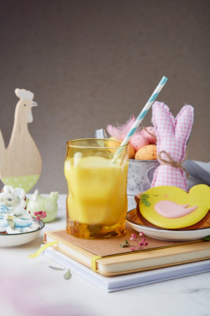 Easter fine art background. Glass of milk and decorated glazed cookies with crafting table...