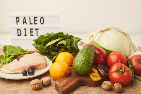 Aesthetics Paleo diet concept with text. Fruits,vegetables, chicken meat, dry fruits, greens on wooden cutting board.の写真素材