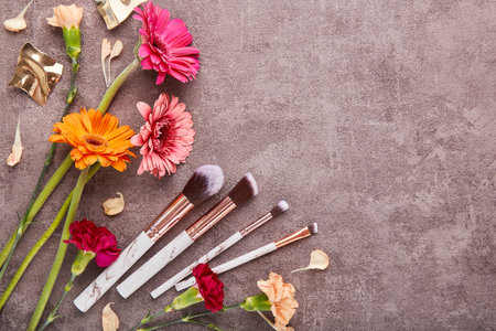 Aesthetic make up brushes set among arrangement of gerbers, asters flowers with copy space. Makeup artist professional tools.の写真素材