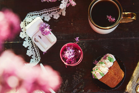 Aesthetic pink floral cupcake, coffee cup on the table. Wireless headphones, listen to music,...