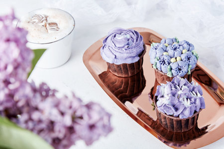 Festive holiday table. Purple french cupcakes on the golden tray. Desserts, coffee and lilac flowers flat layの写真素材