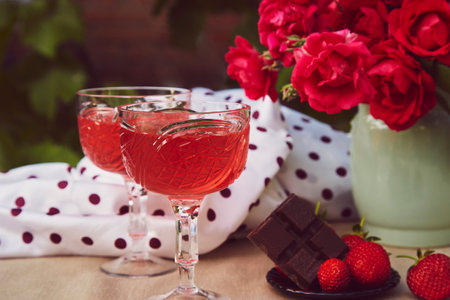 Couple glasses of red sparkling strawberry wine with roses outdoor, strawberry and chocolate. Aesthetic summer table settingsの写真素材