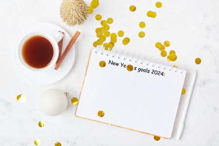 festive desk with a coffee cup, a white mock-up notebook displays New Year's goals 2024