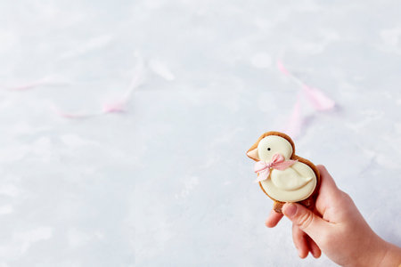 Child hand holds chicken in trendy bow cookie in front of white backdrop. Extra wide banner. Happy Easter background.の写真素材