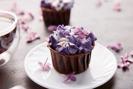 Floral purple cupcake close up using trend Dreamy Escapism. Desserts, coffee and lilac flowers...