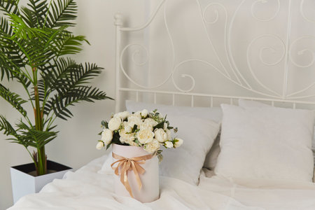 Birthday morning with a gift of fresh white roses in bed. Elegant white bedroom with fresh bouquet and tropical plantの写真素材
