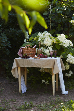 Summer picnic basket with blanket, vintage bottle, fresh fruits, and purple glasses, set against...