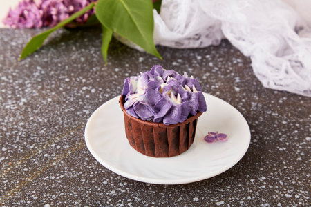 Purple floral cupcake among lilac flowers Spring background. French dessert.の写真素材