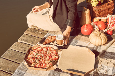Young woman having a dinner outside among autumn decorations, pumpkins, flowers. Autumn picnic ideas on the pier near lake. Fall aesthetics, hard shadows.の写真素材