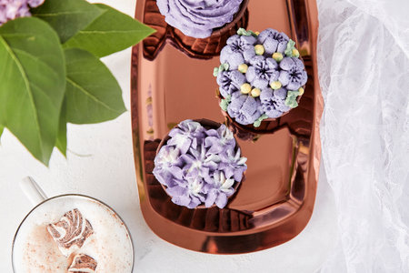 Top view of aesthetics purple floral cupcakes with cup of coffee. No sugar dessert among lilac flowers.の写真素材