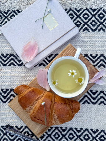 Cup of tea, croissant, and open notebook. Peaceful moment of journaling and presenceの写真素材