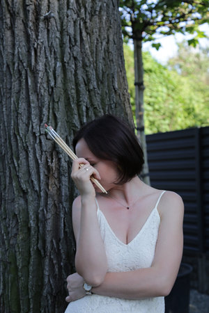 Woman shielding eyes from sun holding paintbrush. Female creative portrait with brush in natural environment.の写真素材