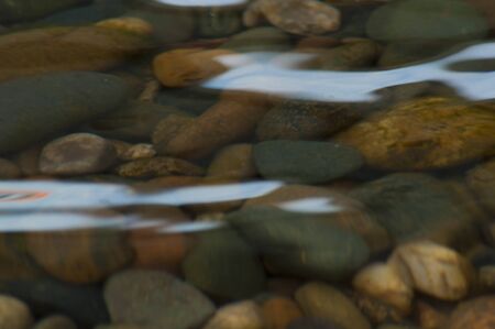 multi-colored pebble under a layer of river water with patches of light