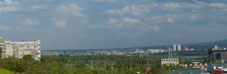 Panorama city a landscape, the houses and high-rise buildings surrounded with trees against the background of the blue skyの写真素材