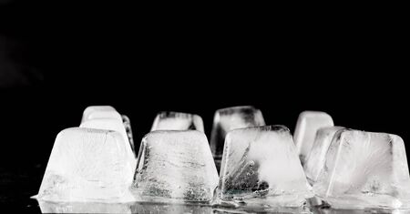 the thawing cubes of ice of white color on a smooth surface, on a black background