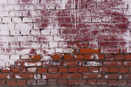 Wall of dark red brick in places painted in white, abstract backgroundの写真素材