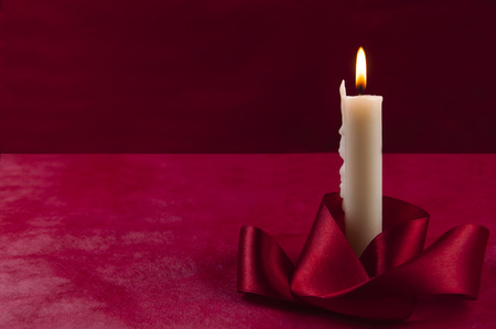 Burning white candle, with red satin ribbon at the bottom, on a red backgroundの写真素材