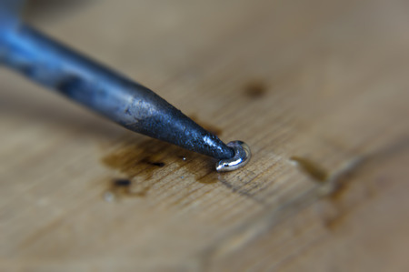 Close-up of melting soldering aluminum wire to the state of liquid metal, on a wooden surface.の写真素材
