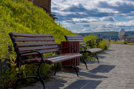 Park benches at the foot of the hill with green grass. Against the blue sky with dark clouds.の写真素材