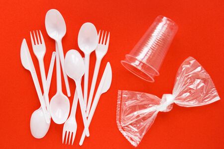 White disposable spoons, forks, knives, glass, package bow on red background close-up - Environmental problem conceptの写真素材