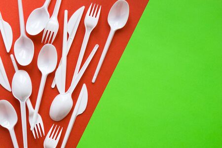 White disposable spoons, forks, knives on red and green background close-up - Environmental problem conceptの写真素材