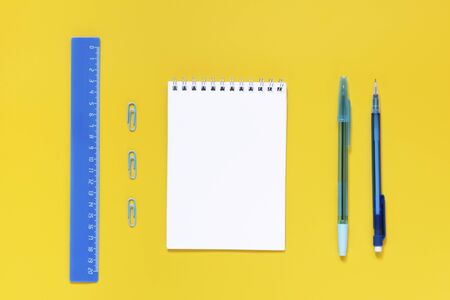 Blue supplies and white notebook in yellow background with copy spice. For right hand. Education, studing, office and back to school concept. Flat lay. School fashion.の写真素材