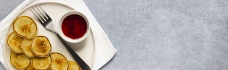 Tiny baked pancakes with berry jam on white plate.