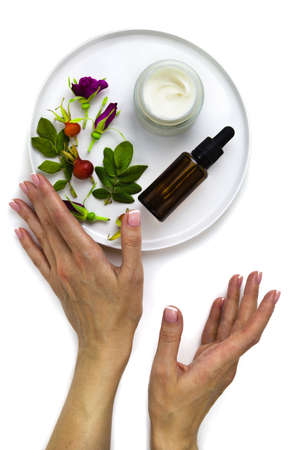 Cream and oil rose hip and female hands on white background. Composition on plate, skin care, flat lay.の写真素材