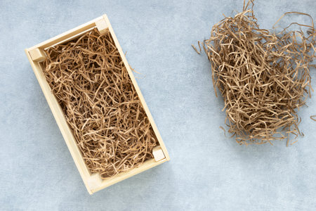 Top view of wooden box for eco gift filled with decorative shredded white paper on gray background.の写真素材