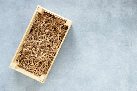 Top view of wooden box for eco gift filled with decorative shredded white paper on gray background...