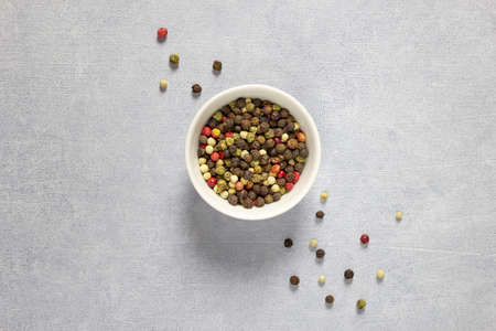 Assorted multicolored colorful papper corn spice in white bowl on grey background.