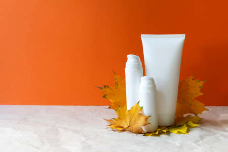 Autumn skin care cosmetic bottles cream yellow fall leaves maple on orange background copy space.の写真素材