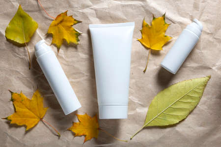 Autumn self care skin face hand or body cream on craft paper background and yellow fall leaves.の写真素材
