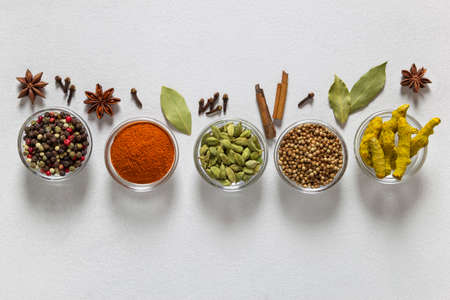 Set of assorted colorful spices in bowls on gray background, flat lay, top view. Cloves, cardamon,...