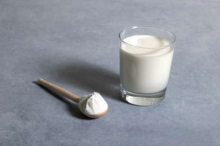 Glass of milk and full fat powdered milk in wooden spoon on gray backgroundの写真素材