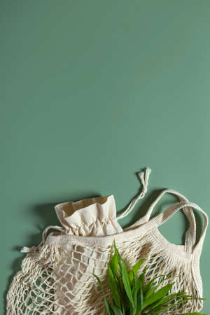 Cotton reusable bag and mesh on green background. Eco-friendly zero waste concept. Copy space.