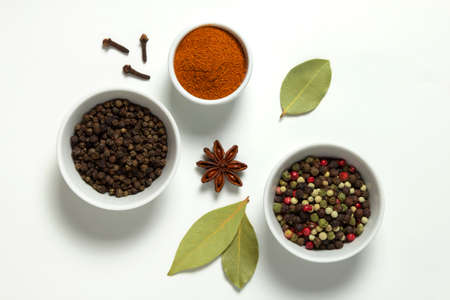 Spices assorted colorful peppercorns and powder paprika in bowls and bay leaf, anise, clove on white...